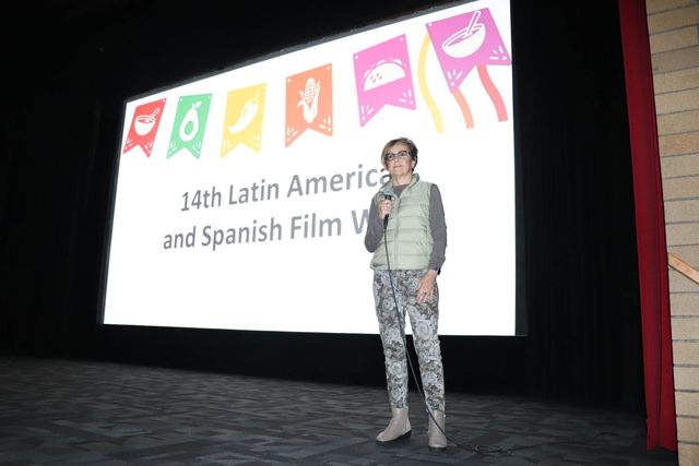 A speaker introducing the festival in front of the projected 14th Film Week title slide